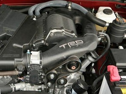 This photos shows an engine compartment with the Toyota Racing Division's Eaton M62 Gen4 IV / Gen5 V Roots-type Twin 3-Lobe Supercharger, found on vehicles equipped with the 4.0 Liter motor, 1GR-FEV6 engine. This is the later generation TRD blower with the black exterior coating, found on vehicles such as the 2007 - 2009 Toyota FJ Cruiser and 2012 - 2015 Toyota Tacoma with the Toyota Racing Division TRD Supercharger Kit.